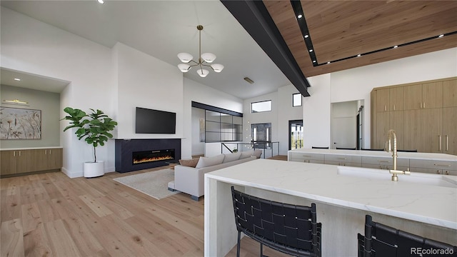 kitchen featuring light wood-type flooring, high vaulted ceiling, pendant lighting, light stone countertops, and beamed ceiling