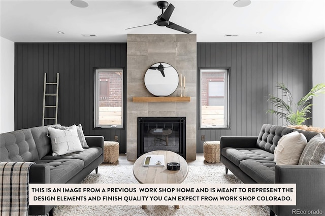 living room featuring wooden walls, a tile fireplace, and ceiling fan