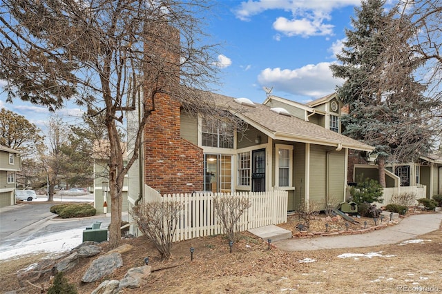 view of front facade with a fenced front yard, a garage, a shingled roof, brick siding, and a chimney