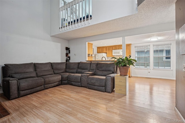 living area featuring a towering ceiling, light wood finished floors, and baseboards