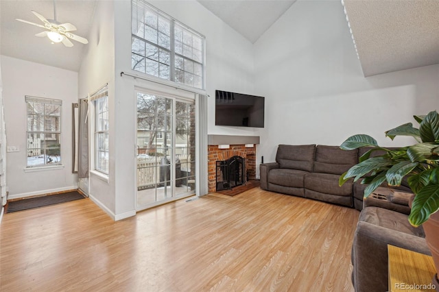 living room with high vaulted ceiling, a brick fireplace, baseboards, and light wood finished floors