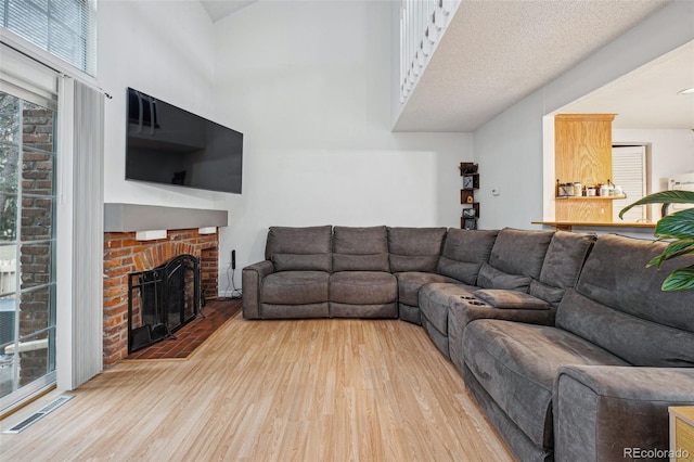 living area featuring visible vents, a fireplace, a towering ceiling, and wood finished floors