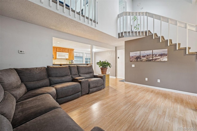 living area featuring light wood-type flooring, baseboards, a high ceiling, and stairway