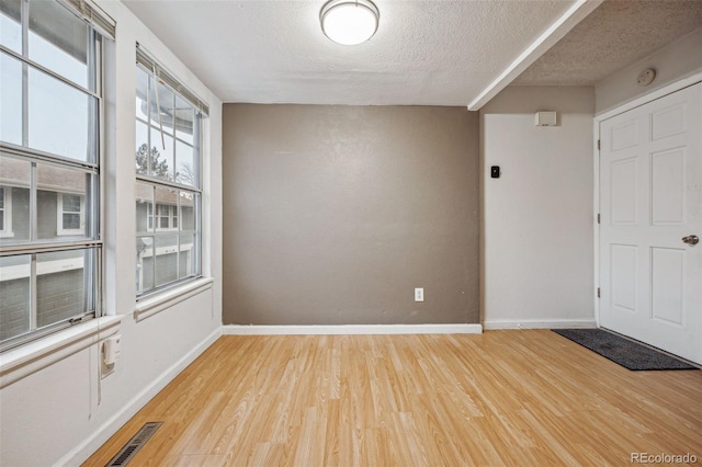 spare room featuring light wood-style floors, baseboards, visible vents, and a textured ceiling