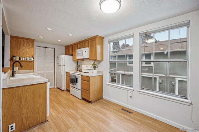 kitchen with light countertops, visible vents, light wood-style flooring, a sink, and white appliances