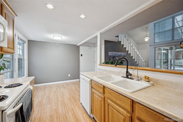 kitchen with white appliances, a sink, baseboards, light countertops, and light wood finished floors