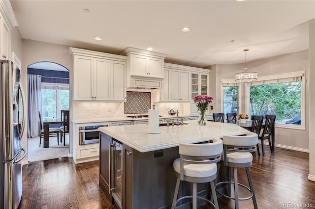 kitchen with white cabinetry, hanging light fixtures, stainless steel appliances, and a kitchen island with sink