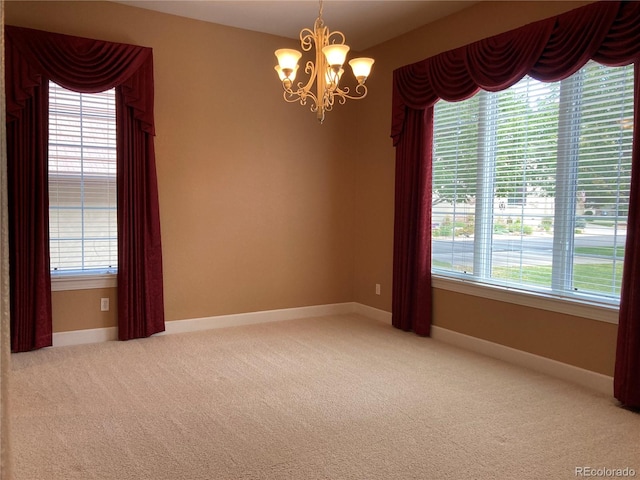 carpeted spare room featuring plenty of natural light and a chandelier