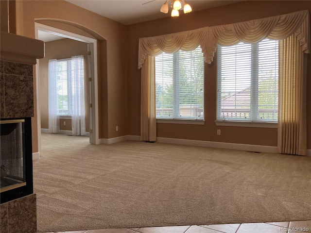 unfurnished living room featuring light colored carpet, plenty of natural light, ceiling fan, and a tile fireplace