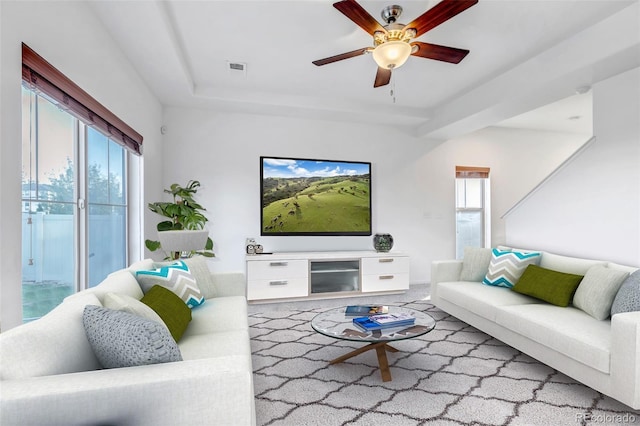 living room with a wealth of natural light, a ceiling fan, and a tray ceiling