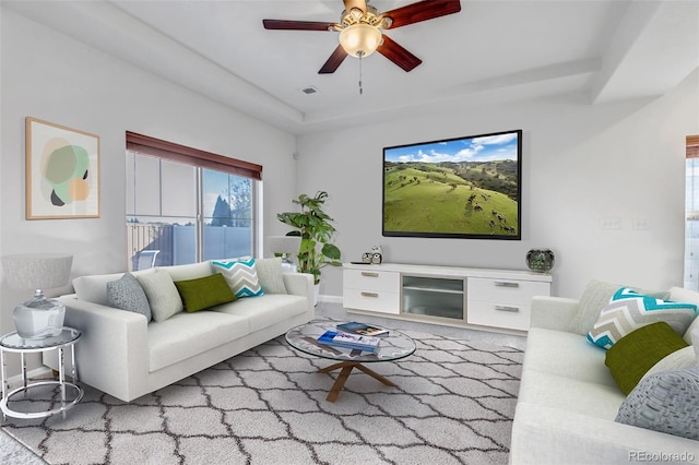 living area with ceiling fan, visible vents, and a raised ceiling