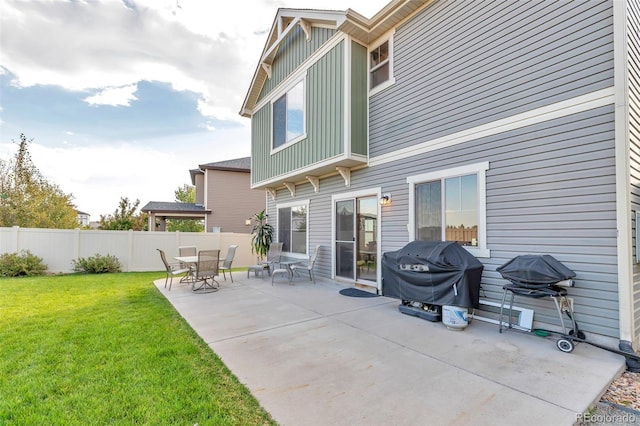 rear view of house featuring board and batten siding, fence, a yard, and a patio