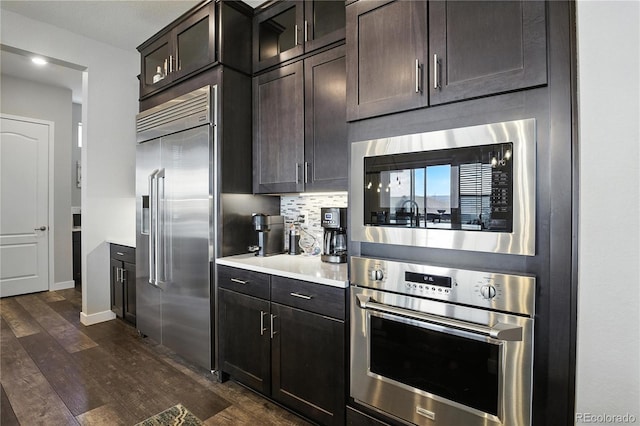 9538 Bear River St, Littleton, CO 80125 - kitchen with appliances with stainless steel finishes, dark wood-style floors, light countertops, dark brown cabinets, and glass insert cabinets