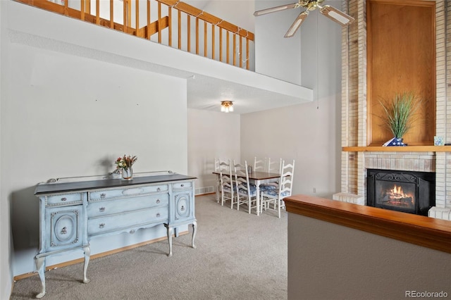 dining space with ceiling fan, light colored carpet, a fireplace, and a high ceiling