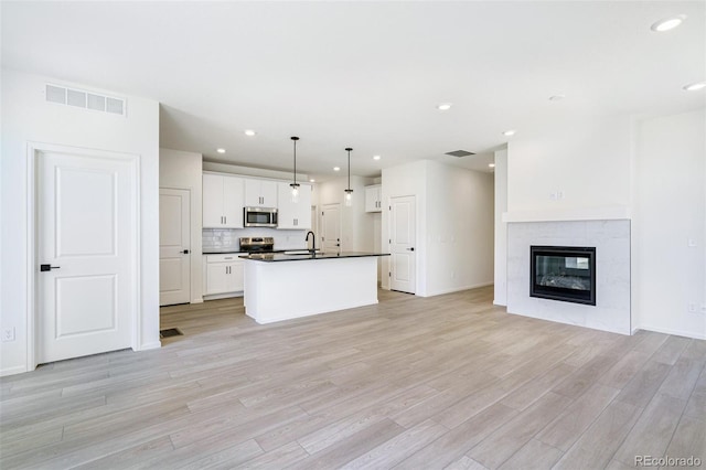 kitchen with appliances with stainless steel finishes, white cabinetry, light wood-type flooring, pendant lighting, and sink