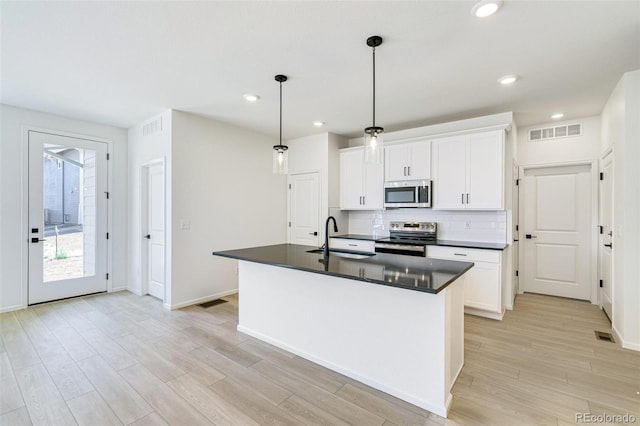 kitchen with a kitchen island with sink, decorative light fixtures, stainless steel appliances, and white cabinets