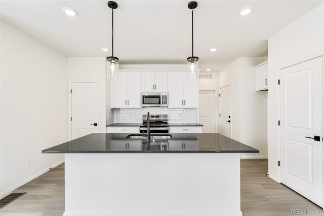 kitchen featuring appliances with stainless steel finishes, decorative light fixtures, and an island with sink