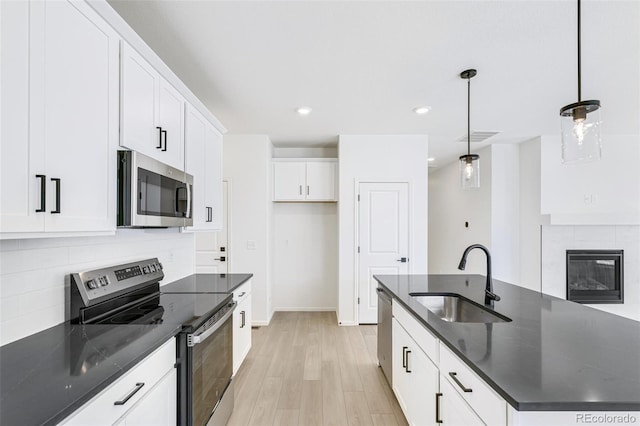 kitchen with appliances with stainless steel finishes, sink, white cabinetry, light hardwood / wood-style floors, and pendant lighting