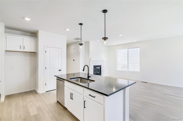 kitchen with stainless steel dishwasher, sink, white cabinetry, and an island with sink