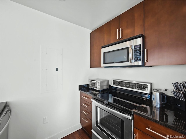 kitchen with stainless steel appliances, dark stone countertops, electric panel, and dark hardwood / wood-style flooring