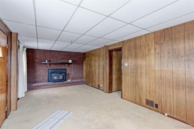 unfurnished living room featuring a paneled ceiling, visible vents, a wood stove, light carpet, and wooden walls