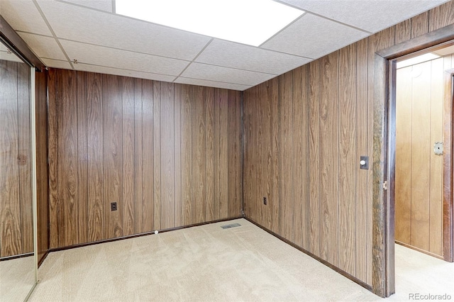 spare room with light carpet, a paneled ceiling, visible vents, and wooden walls