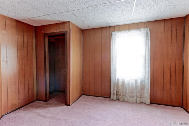 spare room featuring a paneled ceiling, light carpet, and wooden walls