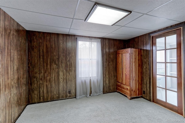 unfurnished room with light carpet, wood walls, and a drop ceiling