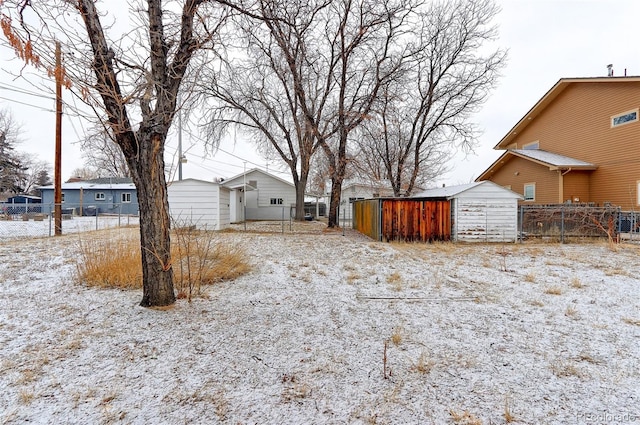 snowy yard featuring a storage shed, fence, and an outdoor structure