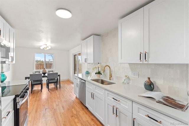 kitchen with a sink, white cabinetry, light countertops, appliances with stainless steel finishes, and backsplash