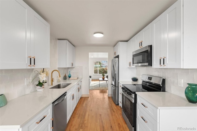 kitchen with stainless steel appliances, light countertops, light wood-style floors, white cabinets, and a sink