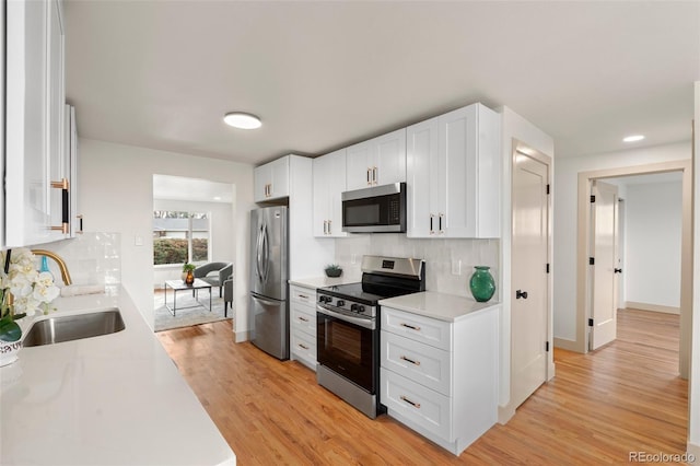 kitchen featuring stainless steel appliances, light countertops, white cabinets, a sink, and light wood-type flooring