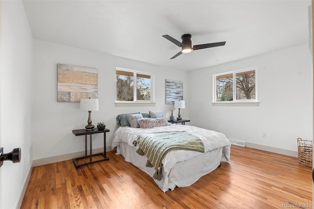 bedroom featuring baseboards, multiple windows, visible vents, and wood finished floors