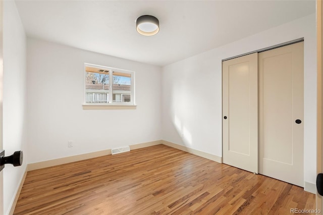 unfurnished bedroom with baseboards, light wood-style flooring, visible vents, and a closet