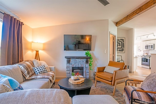 living room with rail lighting, beam ceiling, a fireplace, and light wood finished floors