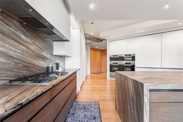 1610 Little Raven St Unit Ph6, Denver, CO 80202 - kitchen featuring wall chimney range hood, decorative backsplash, white cabinets, light wood-type flooring, and recessed lighting