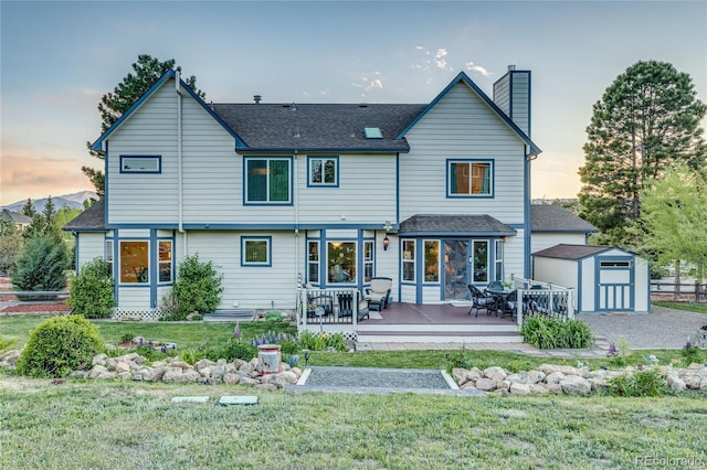 14915 Gleneagle Dr, Colorado Springs, CO 80921 - back of house at dusk with a chimney, outdoor dining area, a lawn, roof with shingles, and a deck