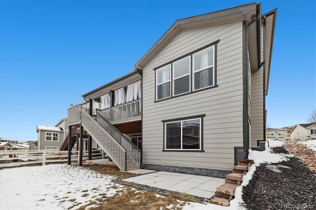 snow covered rear of property featuring fence, a deck, and stairs