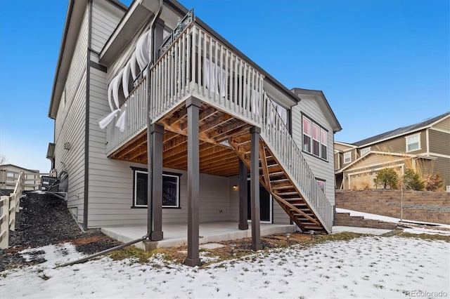 snow covered house featuring a patio, stairway, and fence