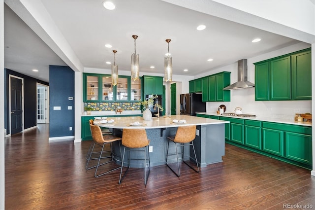 kitchen featuring wall chimney range hood, stainless steel gas stovetop, dark wood finished floors, and black fridge