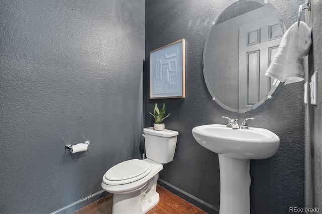 bathroom featuring baseboards, a textured wall, toilet, wood finished floors, and a sink