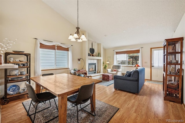 6760 Oakwood Blvd, Colorado Springs, CO 80923 - dining space featuring a chandelier, a fireplace, light wood-style floors, high vaulted ceiling, and a textured ceiling