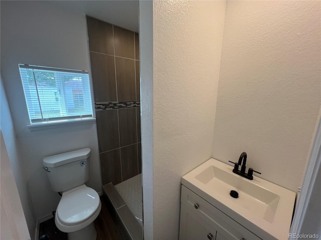 bathroom with a tile shower, vanity, and toilet