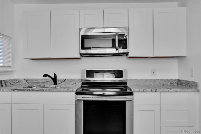 kitchen featuring stainless steel appliances, white cabinetry, light stone countertops, and sink