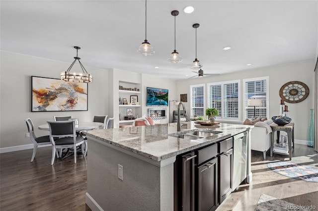 kitchen featuring a kitchen island with sink, sink, light stone countertops, and hanging light fixtures