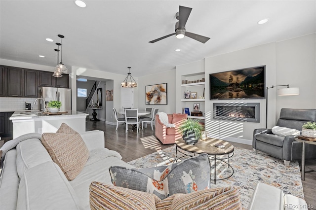 living room with hardwood / wood-style flooring, ceiling fan with notable chandelier, and built in shelves