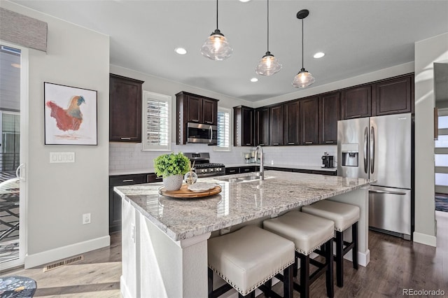 kitchen featuring appliances with stainless steel finishes, sink, light stone counters, dark brown cabinetry, and a center island with sink