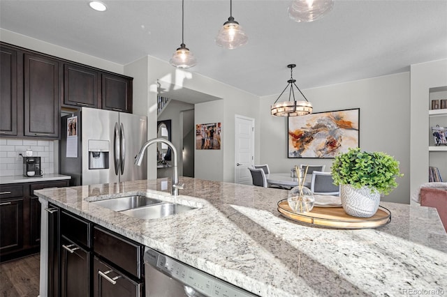 kitchen with stainless steel appliances, light stone countertops, sink, and pendant lighting