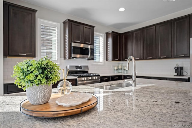 kitchen with sink, dark brown cabinets, stainless steel appliances, light stone counters, and tasteful backsplash