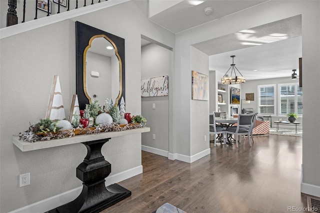 hallway with dark wood-type flooring and an inviting chandelier